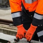 Worker in a hi-vis jacket wearing orange work gloves beside a rail